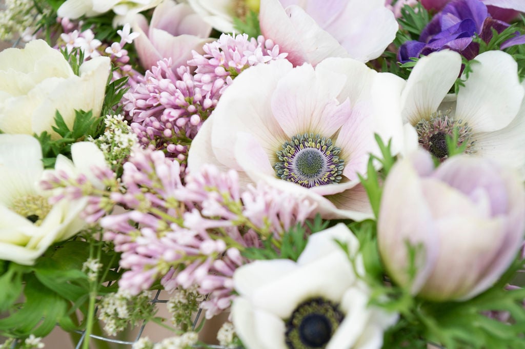 A close-up of a bouquet featuring pale pink and white anemones, light purple lilacs, and green foliage—perfect for those who love to grow spring-blooming flowers in a soft and delicate floral arrangement.